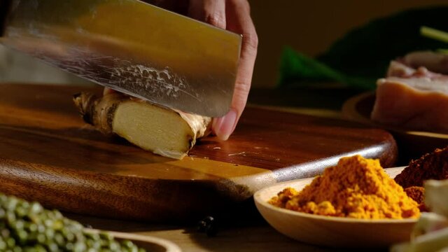 A Motion of chef cutting a ginger in a wooden chopping board and ingredient in kitchen background