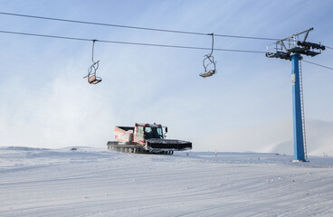 freshly prepared snowy groomed ski trail. tracked vehicle snowcat and lift cables. Winter season, ski resort, cold sunny snowy weather