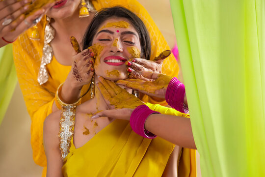 Female hands applying turmeric paste on bride's face on haldi rasam