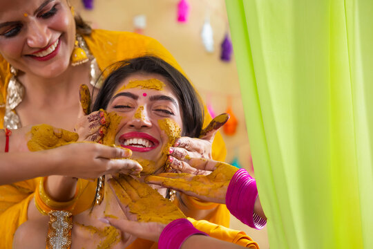 Female hands applying turmeric paste on bride's face on haldi rasam