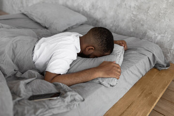 Young African American man sleeping in bed with cellphone