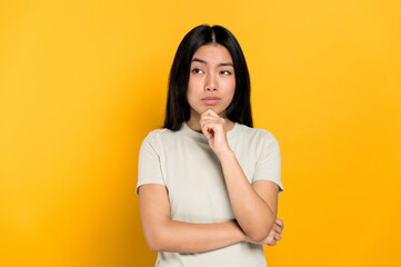 Pensive millennial smart Asian brunette young woman, minded, thinking, creative girl, look up empty space, developing idea, make choice, standing isolated orange background. Copy space