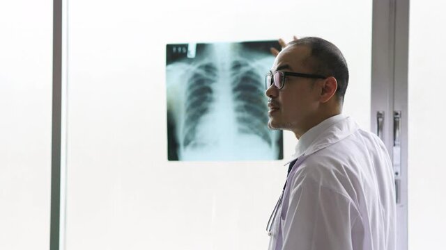 Asian man doctor examining chest x-ray film of woman patient at hospital. Healthcare and medical concept.