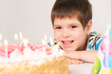 A little boy laughs, celebrates his birthday, sits in front of a white cake with candles.
