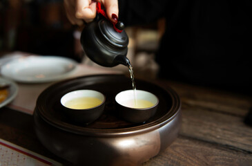 Hot tea with Chinese tea set. A woman pours hot tea from a teapot into cups. A sense of warm comfort. Eco-friendly products and lifestyle.