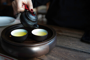Hot tea with Chinese tea set. A woman pours hot tea from a teapot into cups. A sense of warm comfort. Eco-friendly products and lifestyle.