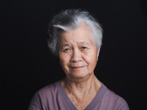 An elderly Asian woman with short gray hair looking at the camera with a smile while standing on black background