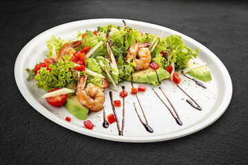 Salad with avocado and tiger prawns, seasoned with pesto sauce. Isolated on a black background.