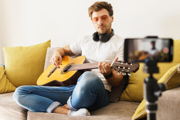 Musician blogger on sofa playing acoustic guitar
