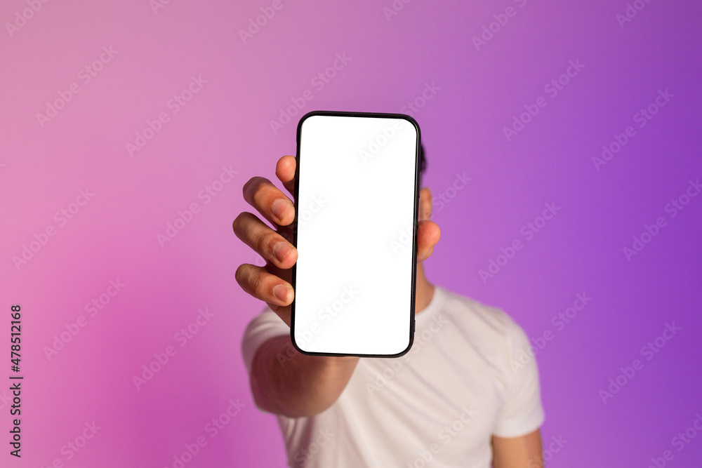 Poster unrecognizable millennial guy holding cellphone with empty white screen in front of his face in neon