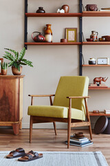 Stylish composition of retro living room interior with design armchair, wooden bookcase, picture frames, plant, carpet, slippers, decoration and elegant accessories in home decor. Template.