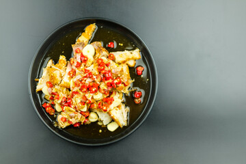 Spicy lime crispy pork salad with sliced red chilli and sliced garlic in a black.