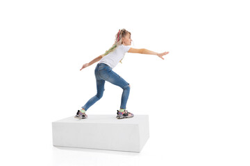 Full-length portrait of smiling girl in casual clothes standing on big box isolated on white studio background. Happy childhood concept.