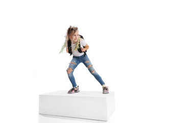 Full-length portrait of smiling girl in casual clothes standing on big box isolated on white studio background. Happy childhood concept.