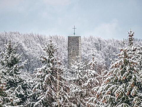 Der Turm der Markuskirche in Bielefeld-Hoberge ragt aus einer schneebedeckten Waldlandschaft heraus