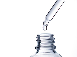 Drop of water falling from glass lab pipette in transparent bottle on white background. Macro