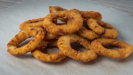 A close-up image for the bar menu. Juicy crispy onion rings lie on a crafting background with parsley leaves.