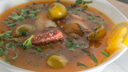 Traditional Russian soup Solyanka with beef, chicken, sausage, lemon, olives and pickled cucumber. Delicious hot lunch.