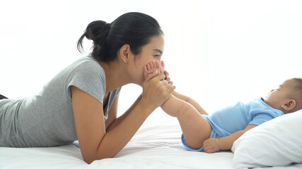 Asian Young mother gently kissing baby's feet sleeping on bed