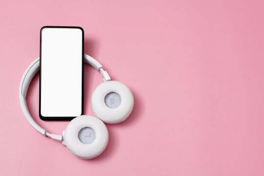 A smartphone with an empty white screen and wireless headphones on a pnik background.