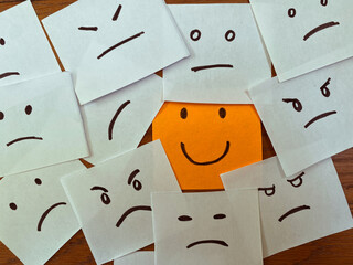 Happy and unhappy facial emotion concept. Happy smiling sticky note among unhappy, sad, angry and emotional face drawings.
