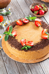 Sweet cake with boiled condensed milk, chocolate and strawberries on a wooden table. Close up view. Bakery food photography.