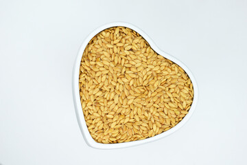 Golden flax seeds in ceramic bowl of heart shape, white background