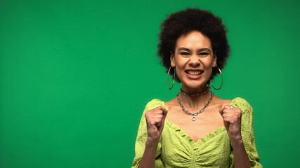 excited african american woman in hoop earrings smiling isolated on green