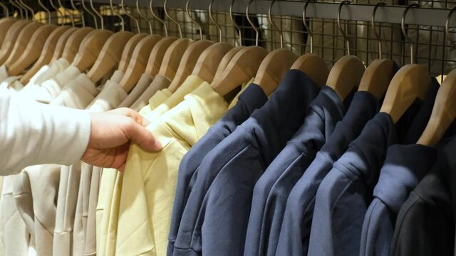 Man chooses colorful hoodies hanging on hangers in clothing store.
