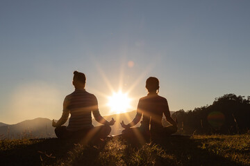 Silhouette of Mother and daughter doing yoga on mountain outdoors in summer park at sunset