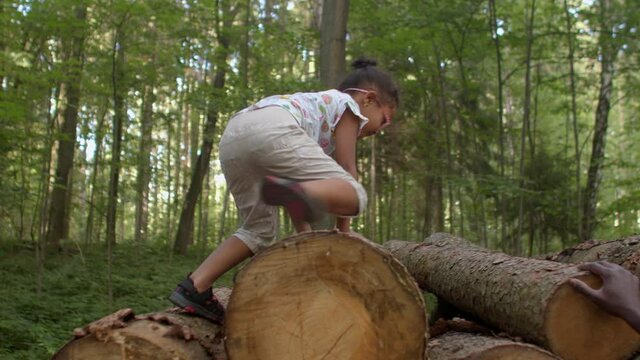 A girl climbs the stacked logs playing with dad in the park. Stacking firewood is to keep it in a manageable height. Wood is very heavy and can fall off and injure people. Dangers of firewood stacks.