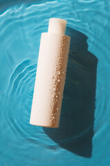 white blank bottle for cosmetics, shampoo, hair products on blue background in water