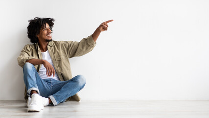 Check This. Positive African American Guy Sitting On Floor And Pointing Aside