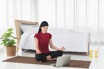 Asian woman, attractive and young, is practicing yoga by studying online classes, in her white bedroom, concept to new normal and education online