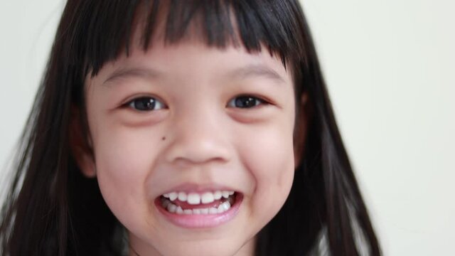 Video 4K Portrait of a Thai Asian kid girl aged 4 to 6 years old, cute looking, playing with his hands and eyes closed. and opened his face happily and joyfully, his eyes sparkling with good health.