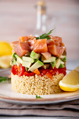 Salmon tartare with tomatoes, avocado and quinoa on a plate and light gray table close up, vertical photo