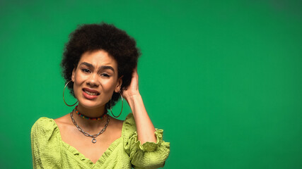 confused african american woman scratching head isolated on green