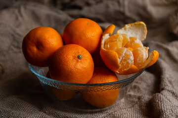 juicy orange tangerines in a glass vase on a burlap background, one peeled