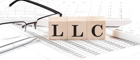 LLC written on wooden cube with keyboard , calculator, chart,glasses.Business concept