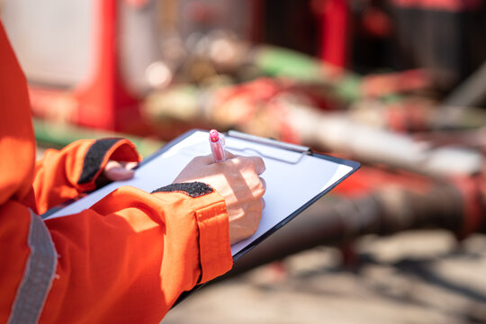 Safety officer or Supervisor is writing note on the checklist paper during perform audit and inspection in oil field operation. Close-up action and selective focus photo.