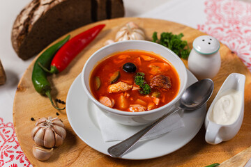 solyanka national team. a portion of spicy red hot soup with tomatoes, sausages and olives on a wooden background