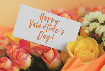 bright bouquet of orange and yellow roses with white gift card and inscription happy valentine's day, 14 february holiday concept
