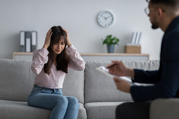 Upset and depressed arab woman touching head, seeking professional help at psychotherapist's office