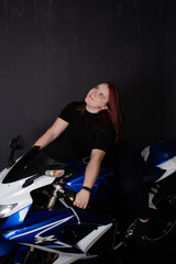 Fototapeta na wymiar redhead girl in black posing on blue motorcycle on black background. woman female moto-driver portrait.