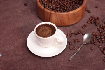 Coffee beans in a wooden plate and a cup of brewed coffee on a brown background