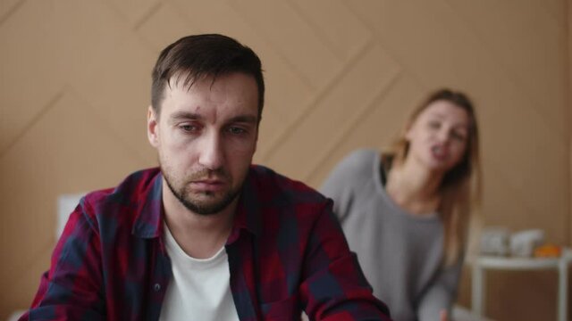 Man is sitting on bed with sad face, girlfriend is talking to him and hugging comforting, front view. Distressed husband sitting on bed, wife trying to comfort him. Support concept