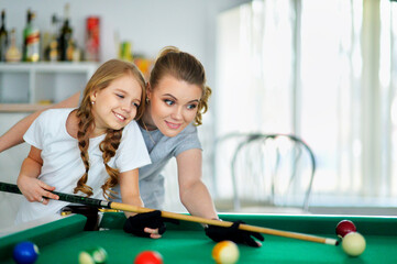 Fototapeta premium Portrait of little cute girl with mother playing billiards