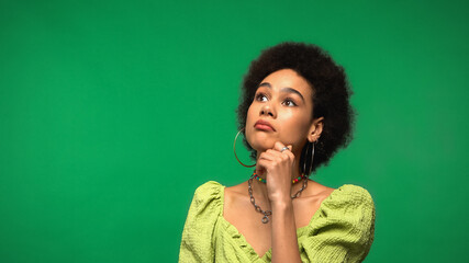 pensive african american woman in hoop earrings and blouse looking away isolated on green