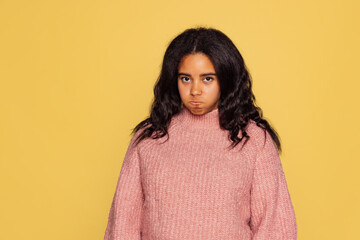 Fototapeta premium Half-length portrait of young pretty dark skinned girl in warm knitted sweater isolated on yellow background.