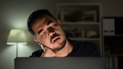 Overworked tired, Asian businessman sleeping while using computer working late at night at home